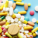 An assortment of pills in various shapes, sizes and colors scattered on a pale blue backdrop.